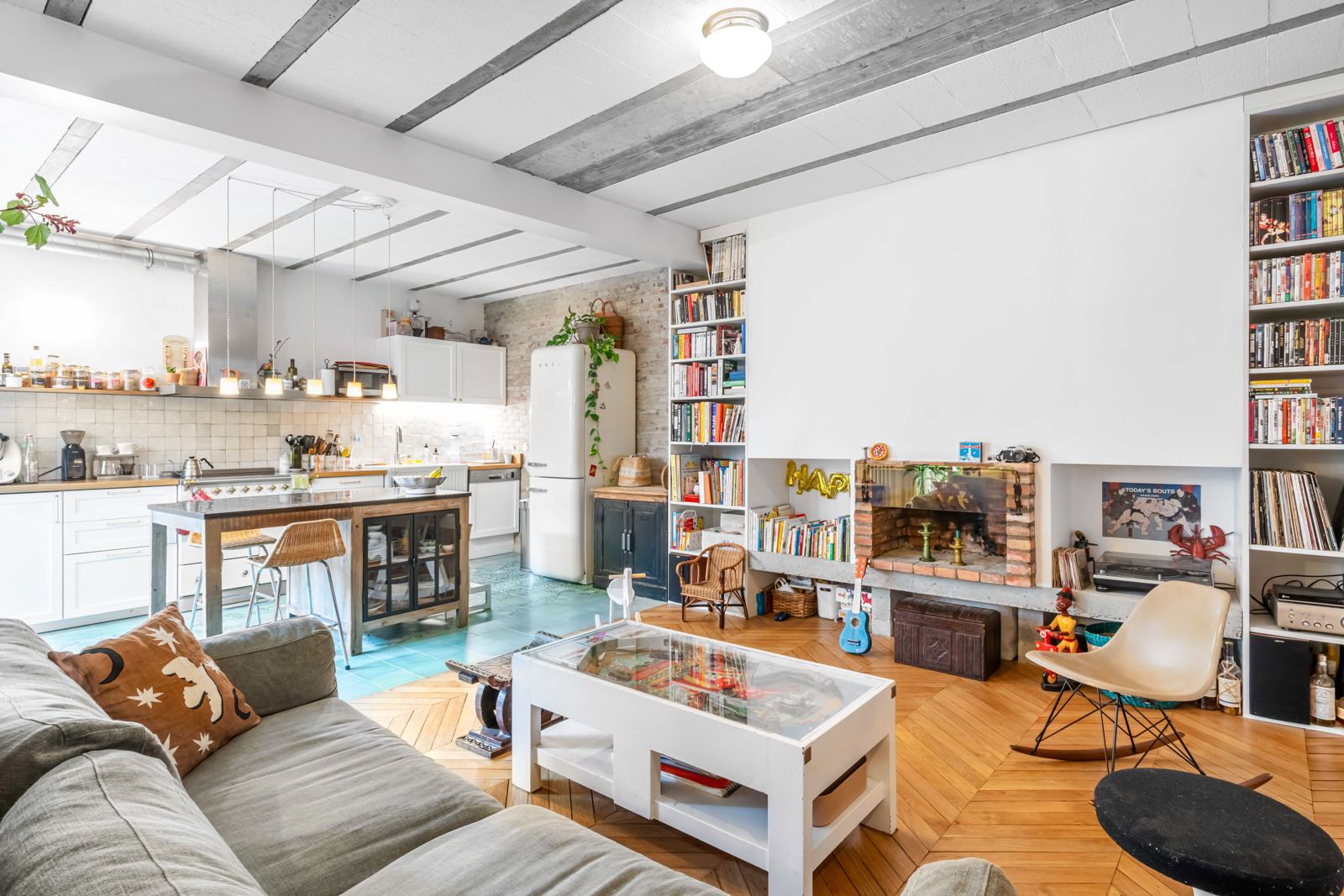 Salon avec cheminée en briques, bibliothèques et cuisine ouverte