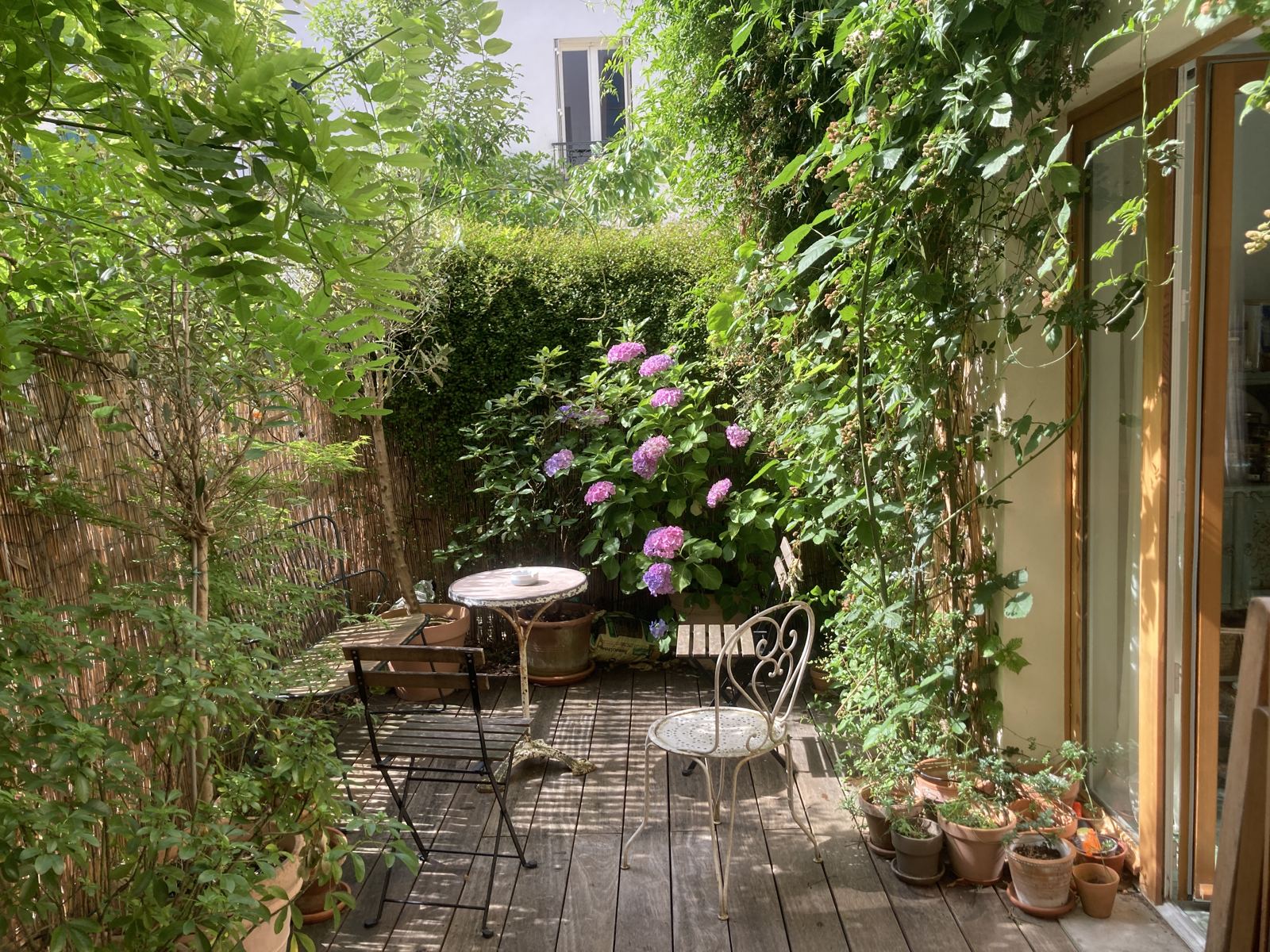 Terrasse privée en bois, plantes grimpantes, hortensias et mobilier de bistrot